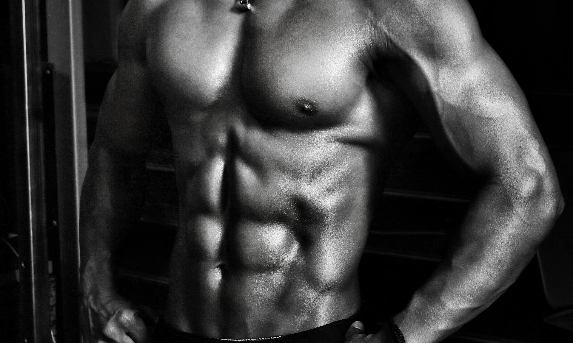 Black and white image of a shirtless man wearing shorts with strong abs on a black background