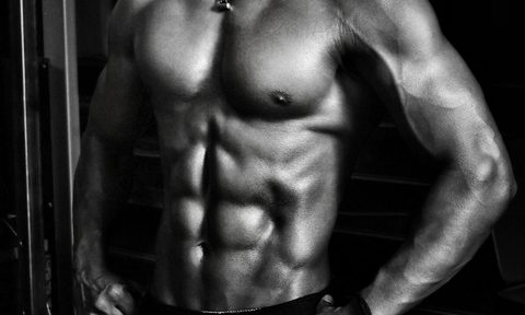 Black and white image of a shirtless man wearing shorts with strong abs on a black background