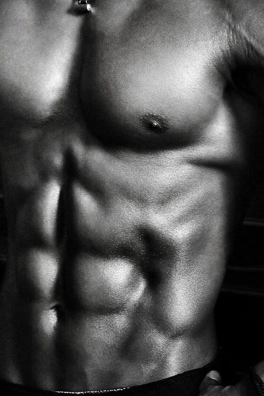 Black and white image of a shirtless man wearing shorts with strong abs on a black background