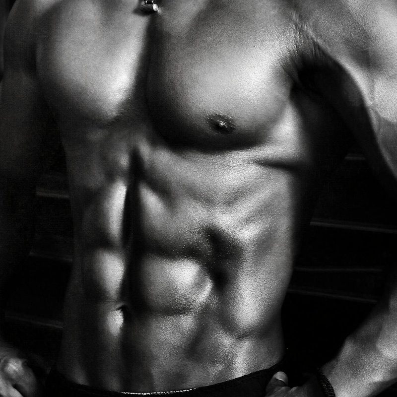 Black and white image of a shirtless man wearing shorts with strong abs on a black background