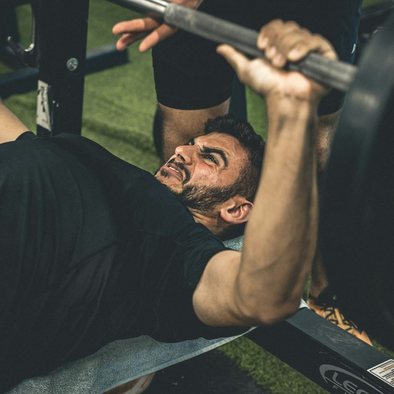 man wearing black shirt laying on bench in gym lifting weights