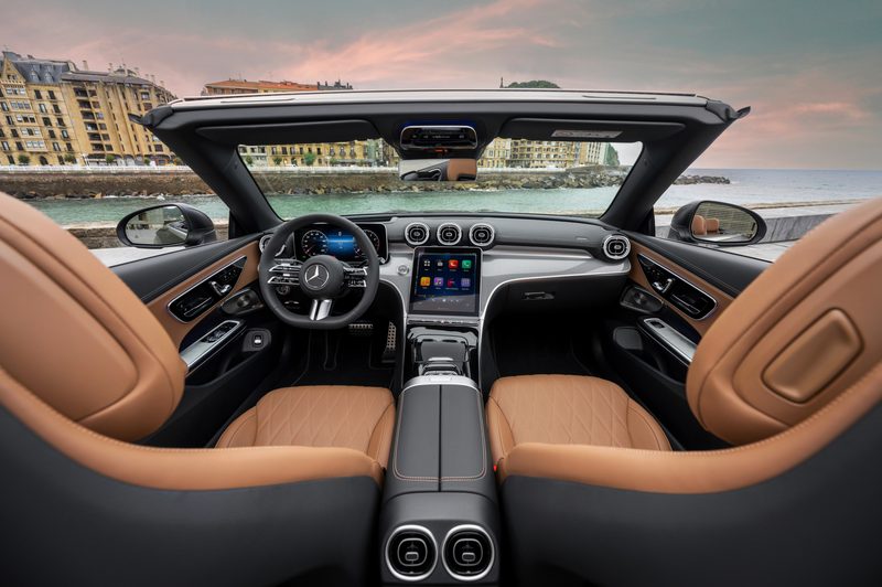 2024 Mercedes-Benz CLE Cabriolet in gray with tan upholstery top down front seating and dashboard image taken from the back with water and European buildings.