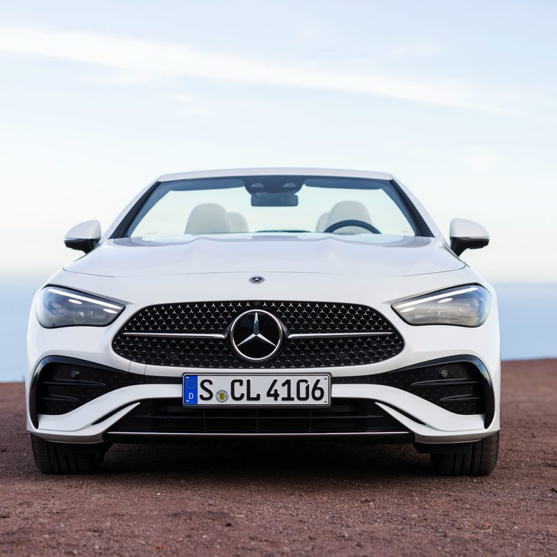 2024 Mercedes-Benz CLE Cabriolet in white direct frontal view parked on red ground with clouds and sky in the background.