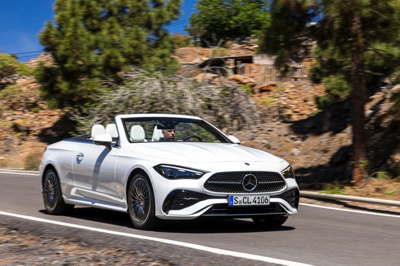 2024 Mercedes-Benz CLE Cabriolet in white right front three-quarter view of a person driving on a paved road with the top down.