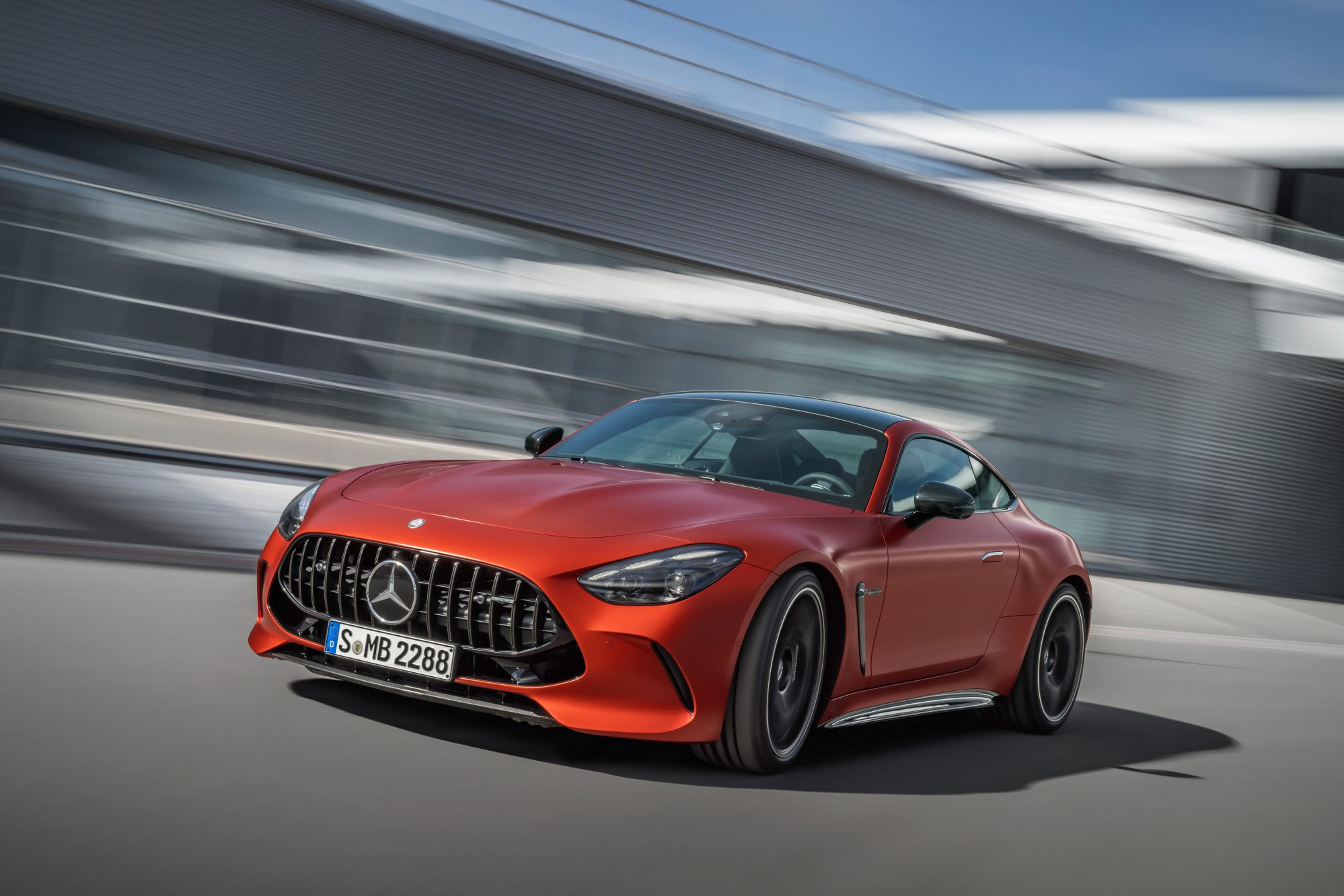 2025 Mercedes-AMG GT 63 S E Performance left front three-quarter view driving in front of a glass-walled building.