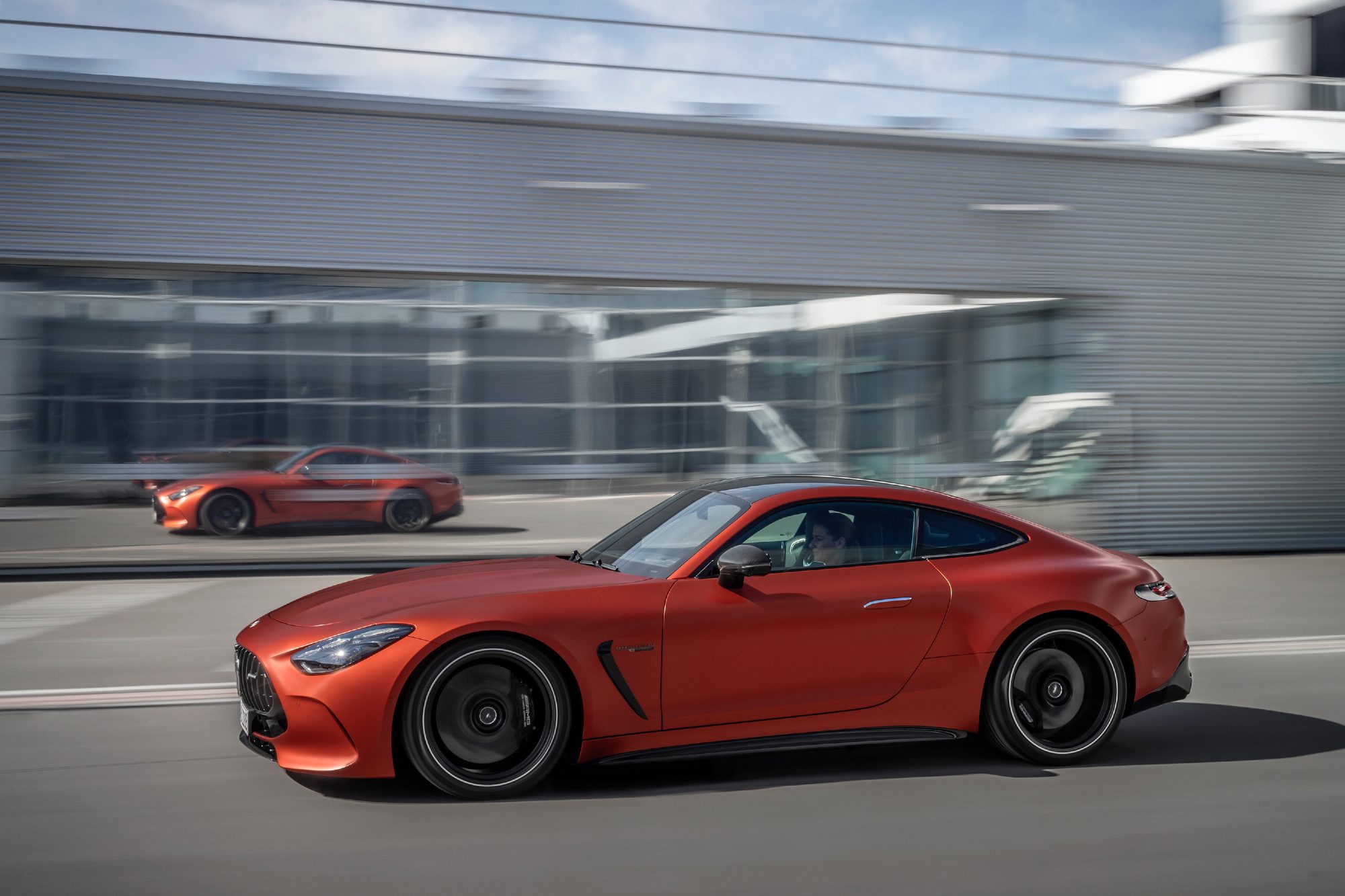 2025 Mercedes-AMG GT 63 S E Performance left profile driving in front of a glass-walled building.