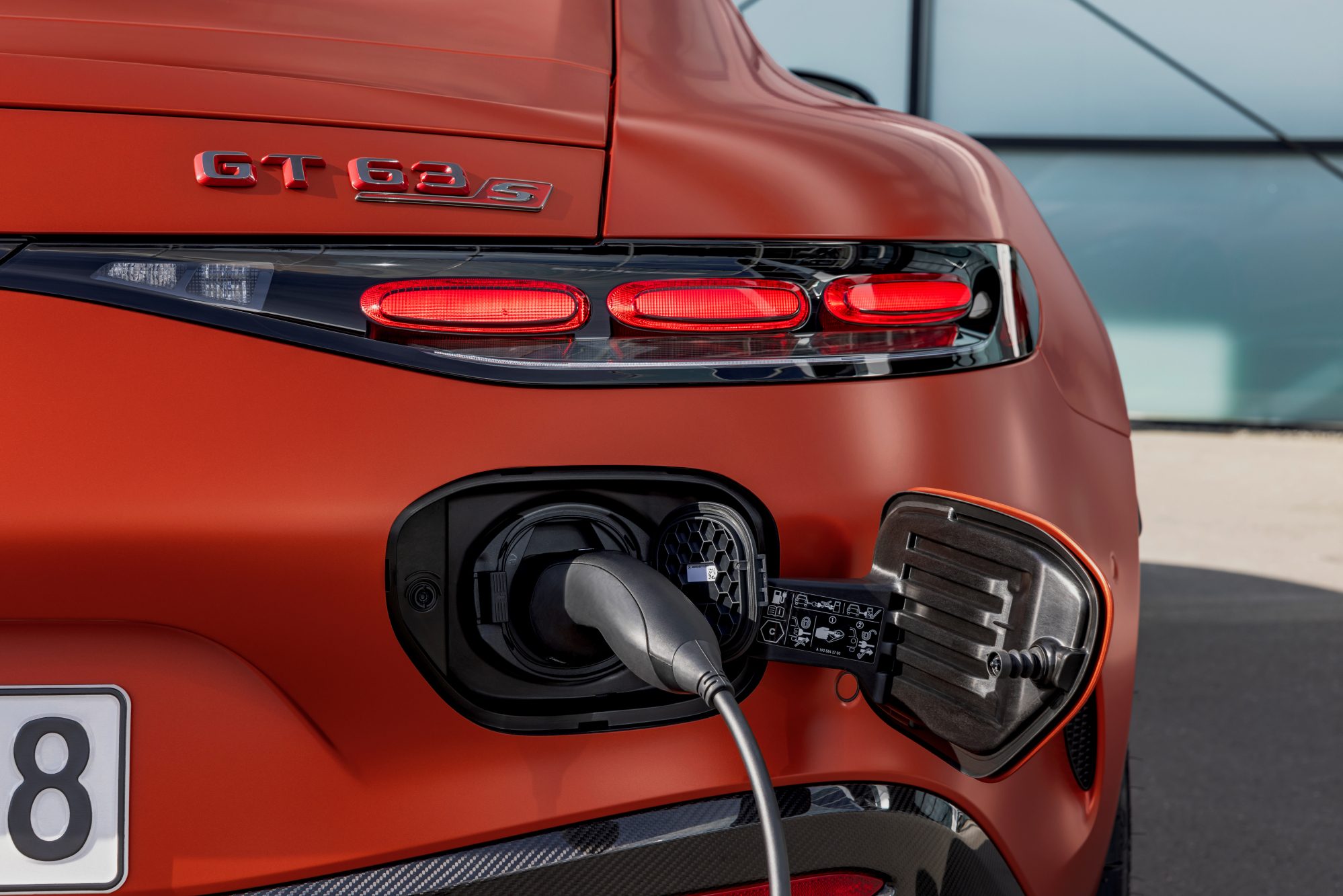 2025 mercedes amg gt 63 s e performance right rear with charging cable plugged in parked front of a glass walled building