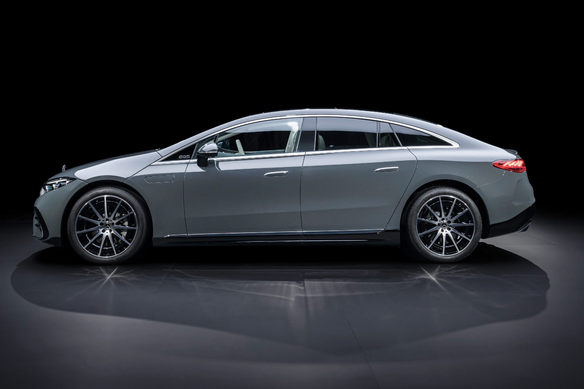 2025 Mercedes-Benz EQS in MANUFAKTUR Signature Silicon Grey direct left profile view on gray reflective flooring and a black background.