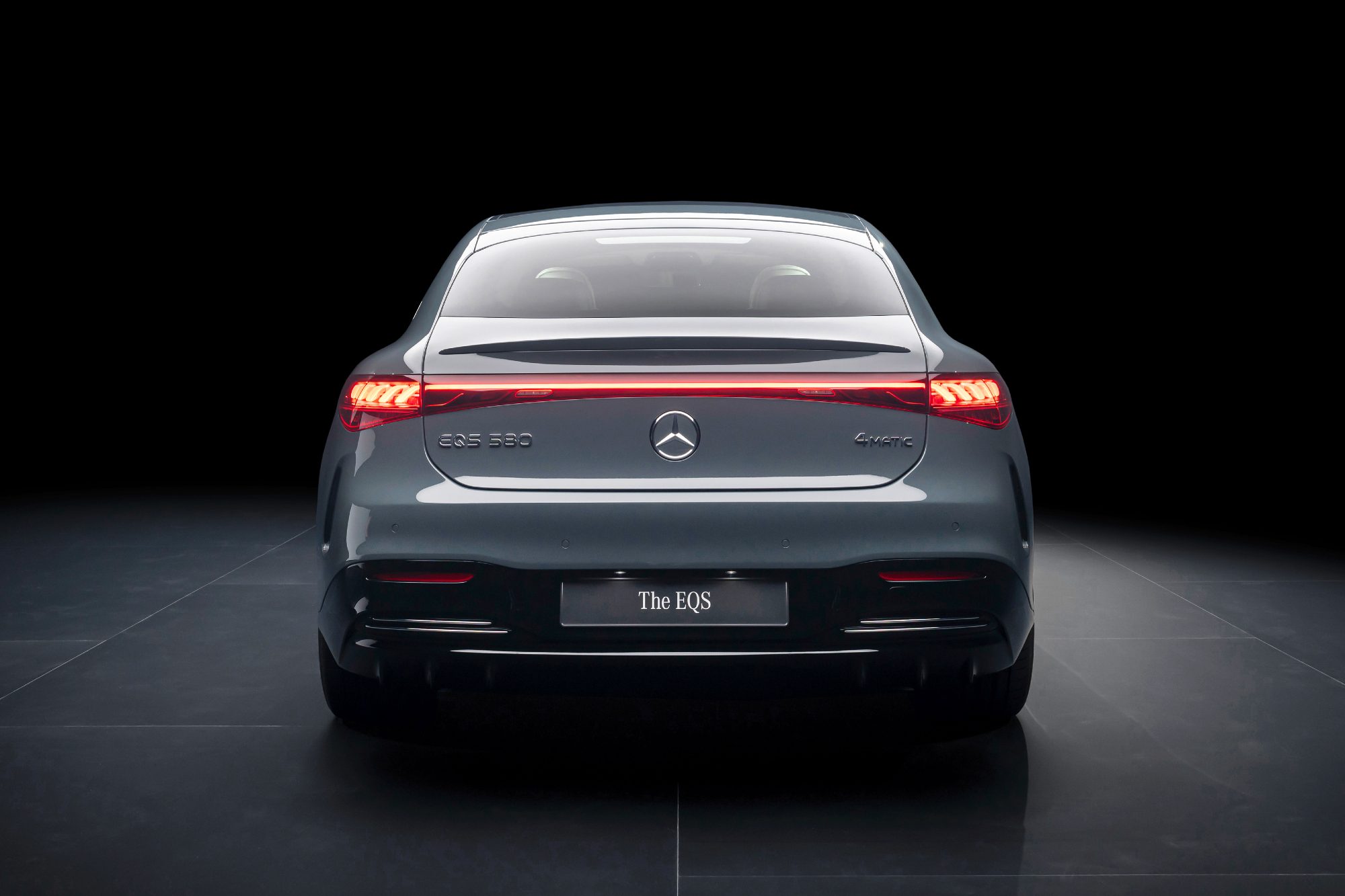 2025 Mercedes-Benz EQS in MANUFAKTUR Signature Silicon Grey direct rear view on gray reflective flooring and a black background