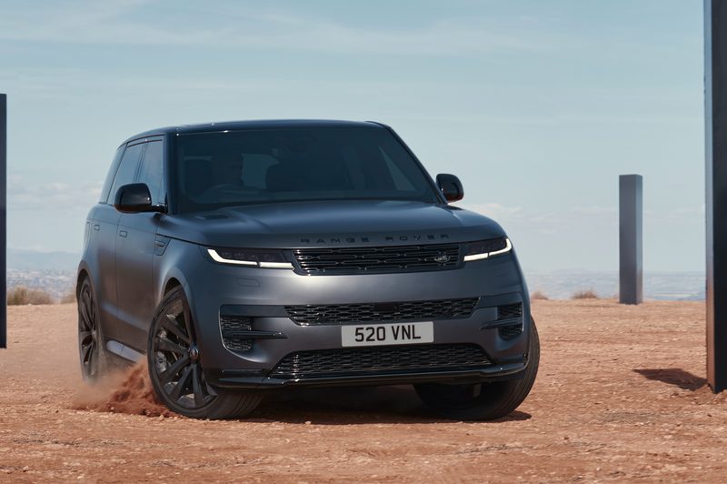 025 Range Rover Sport Dynamic SE with Stealth Pack sliding into a left turn on desert sand with black monoliths in the background.