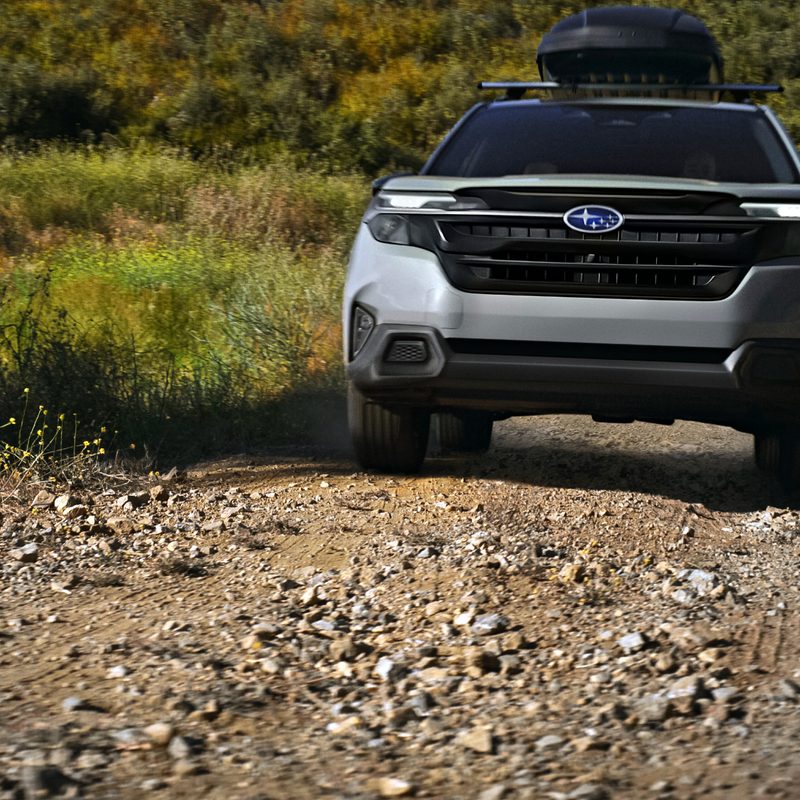 2025 Subaru Forester driving up a rock-strewn dirt road with a luggage case on the roof rack.