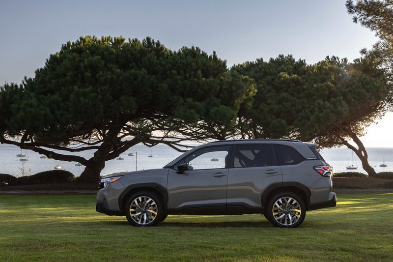 2025 Subaru Forester parked on grass with trees and distant water in the background.