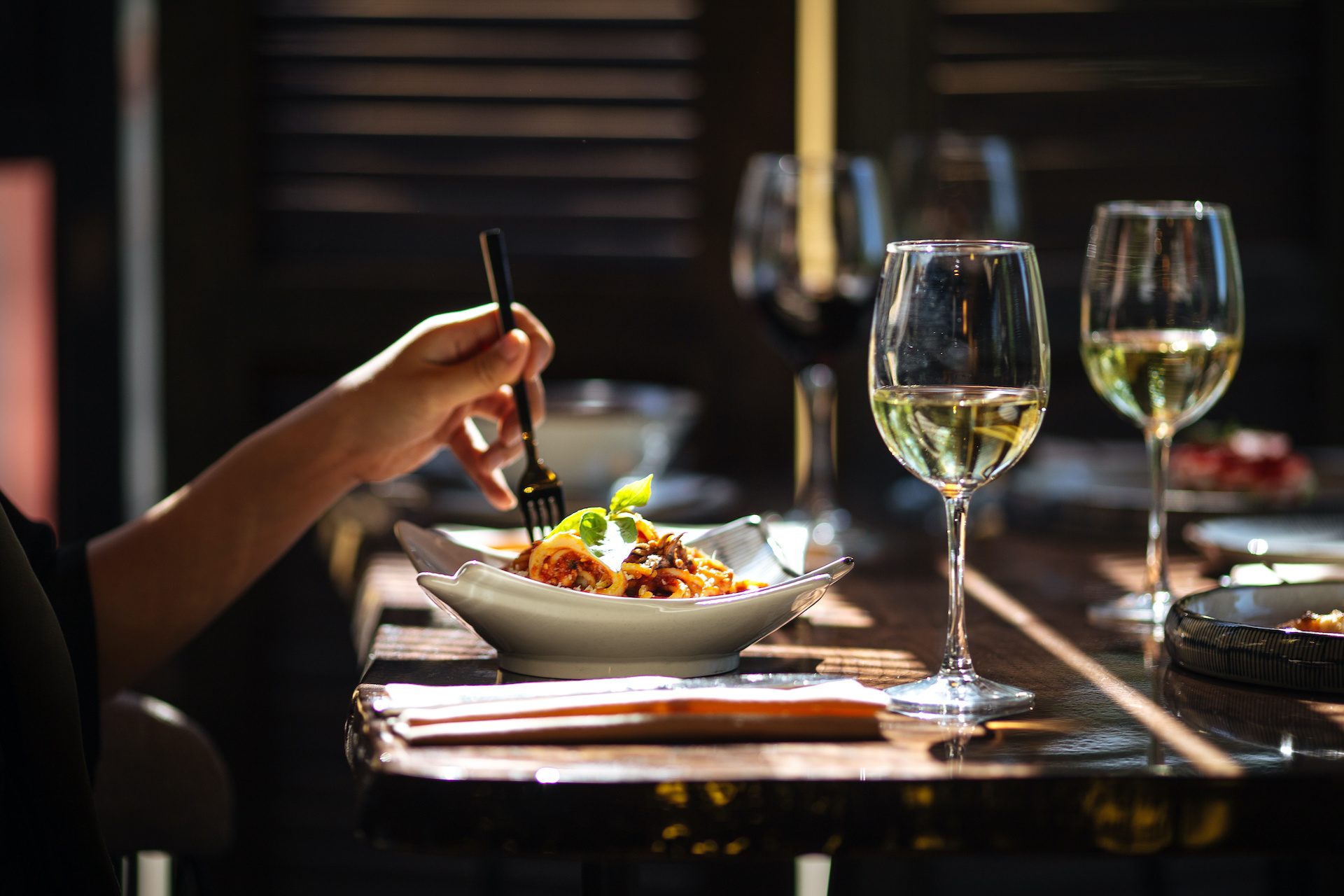 Person eating in restaurant with plate and white wine