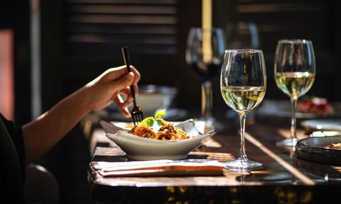 Person eating in restaurant with plate and white wine