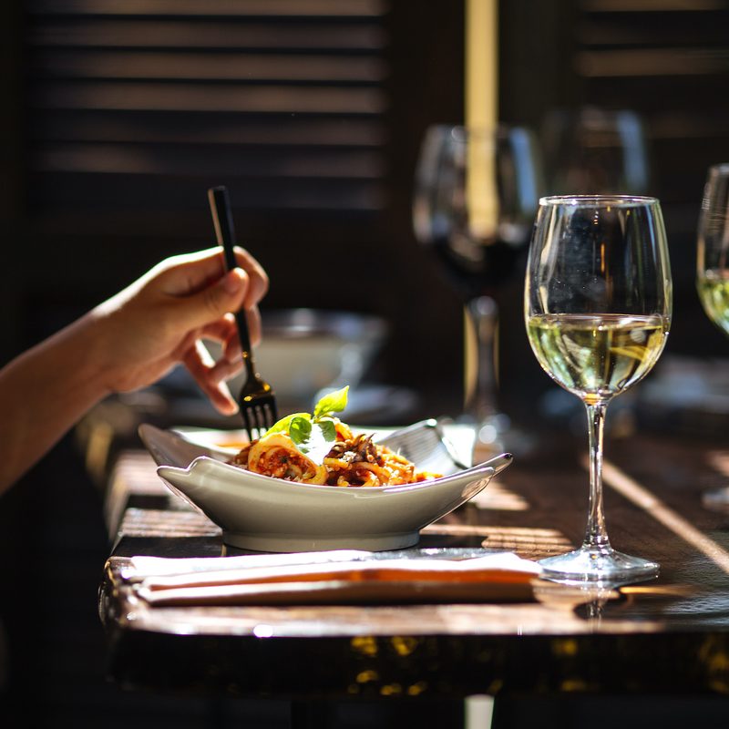 Person eating in restaurant with plate and white wine