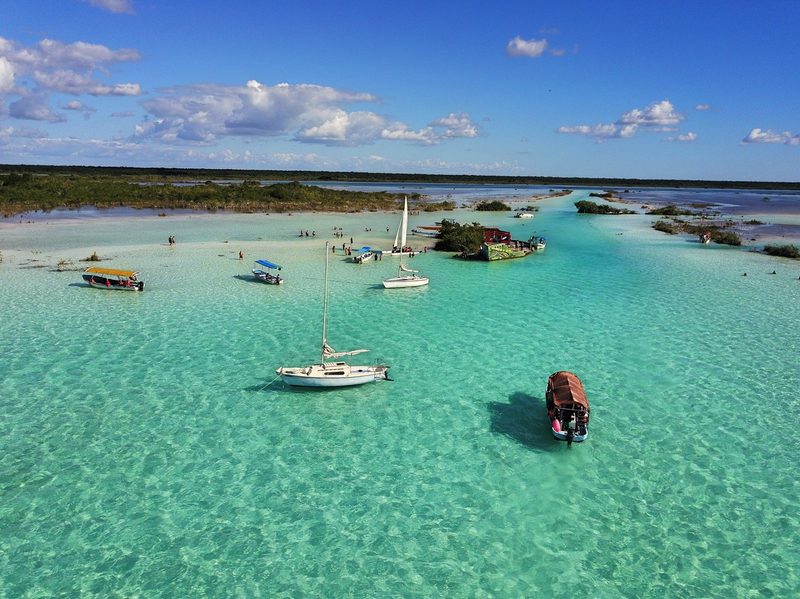 aerial view of turquoise pirates channel at Bacalar Lagoon with boats and sandbars, blue sky, white clouds