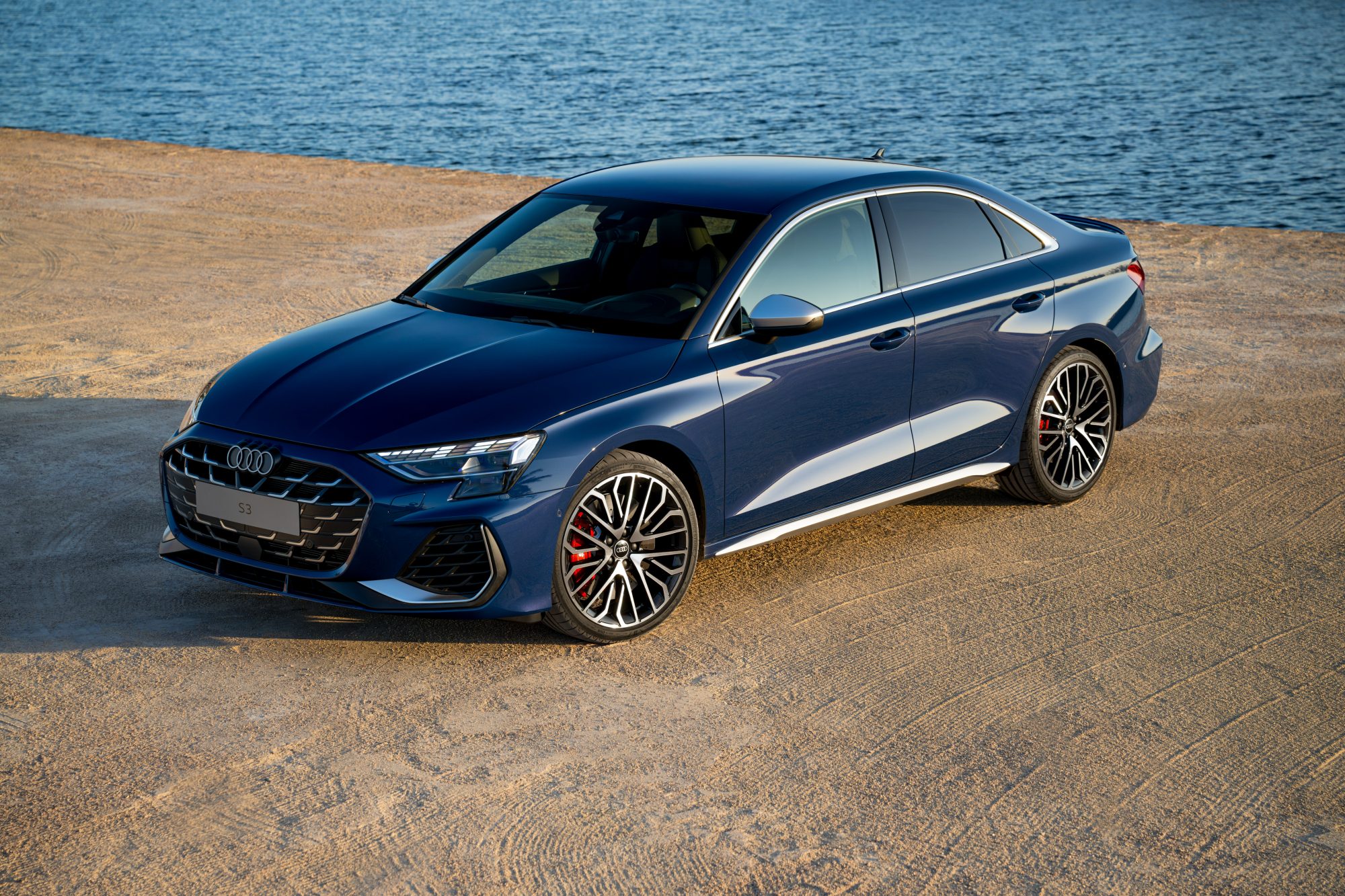 Blue 2025 Audi S3 left front three-quarter view parked on a beach with water in the background.