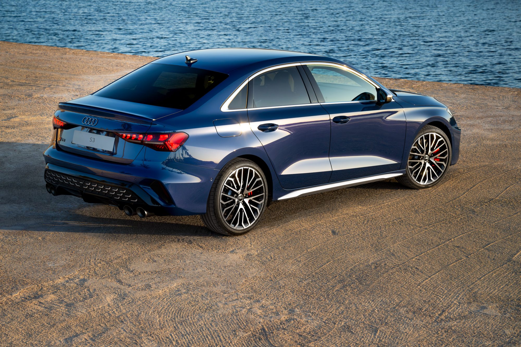Blue 2025 Audi S3 right rear three-quarter view parked on a beach with water in the background.