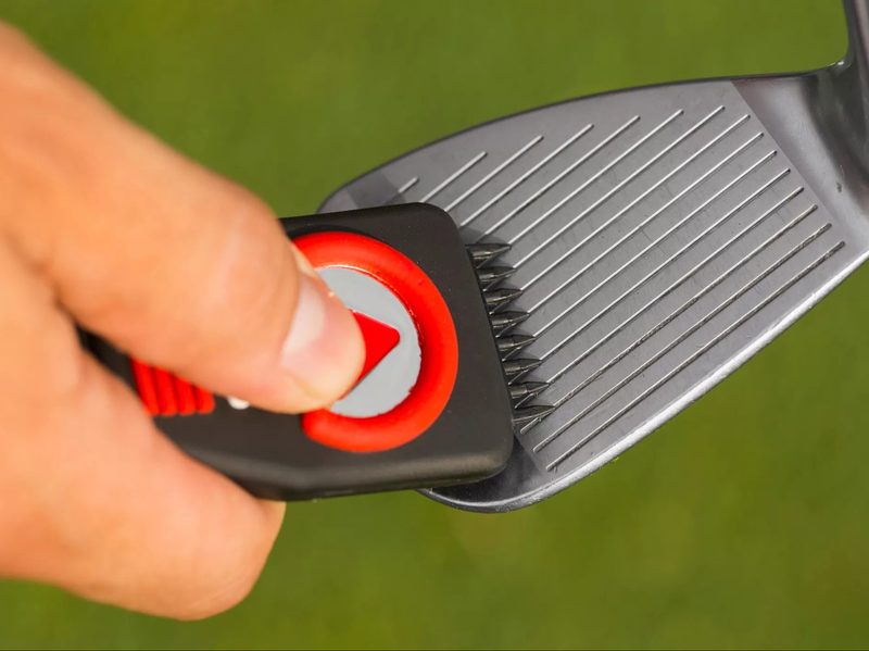 A man using the Callaway Clean N' Cut Groove Cleaner's brush on his golf club.