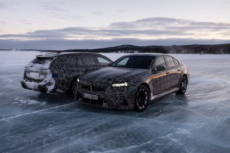 Camoflaged 2025 BMW M5 Sedan and M5 Touring European models parked side by side on ice on a huge body of water.