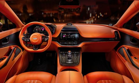 Front seat interior shot of seats and dashboard of Aston Martin DBX707 with blurred city street lights visible through the windshield.