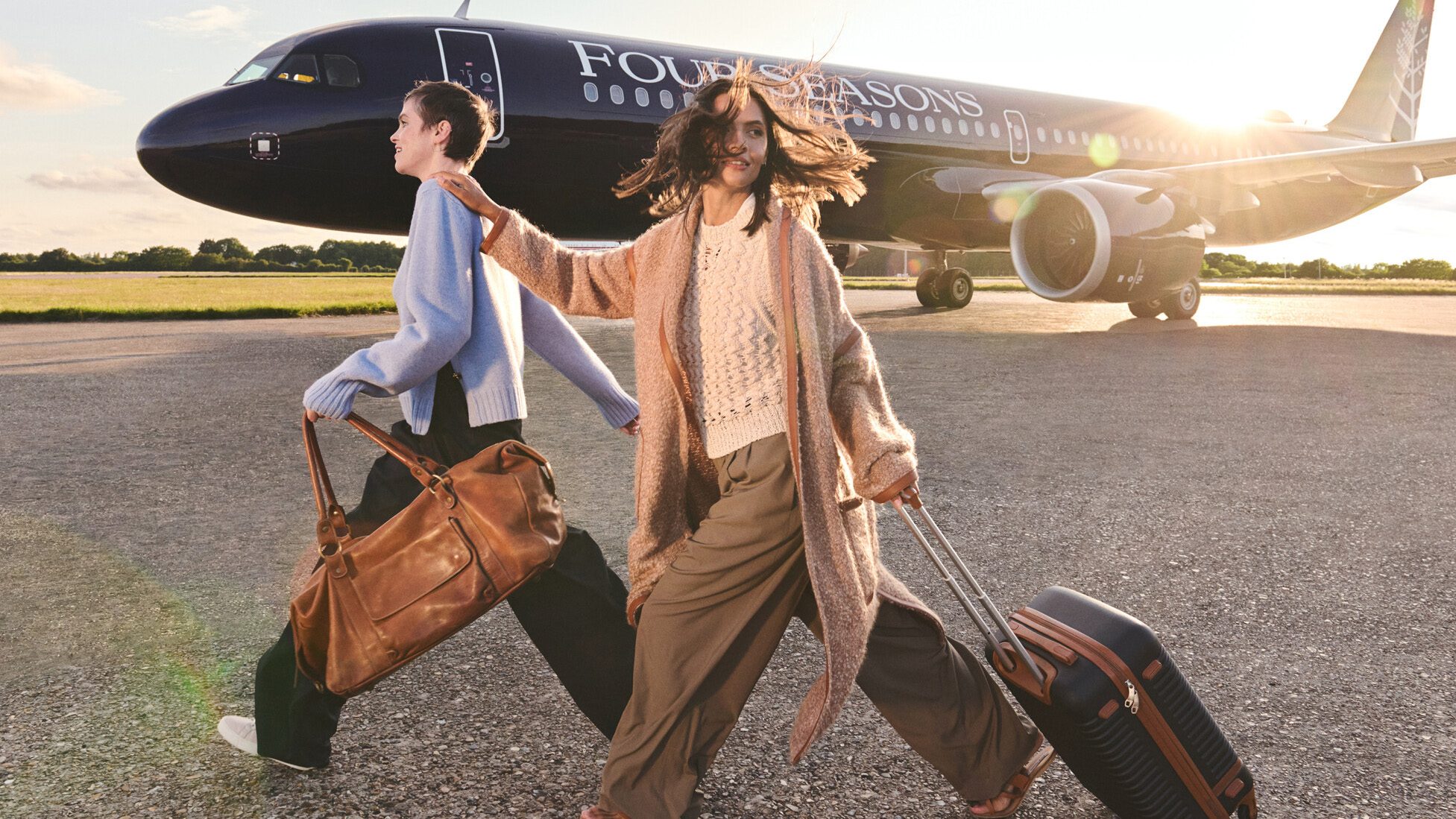 people walking in front of the Four Seasons jet with luggage in hand