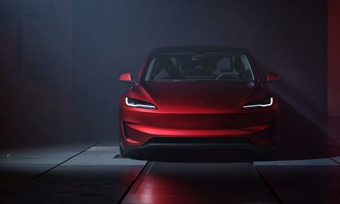 Red Tesla Model 3 Performance facing straight on parked on dark metal plates with a dark wall in the background.