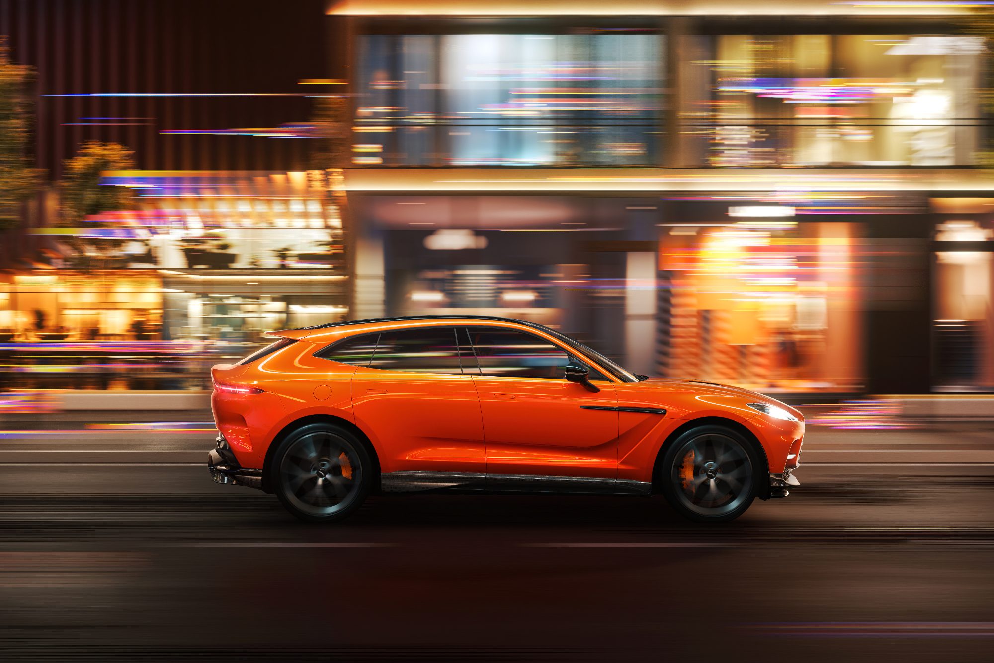 Right profile of a new Aston Martin DBX707 on a city street with blurred lighting as car drives from left to right.