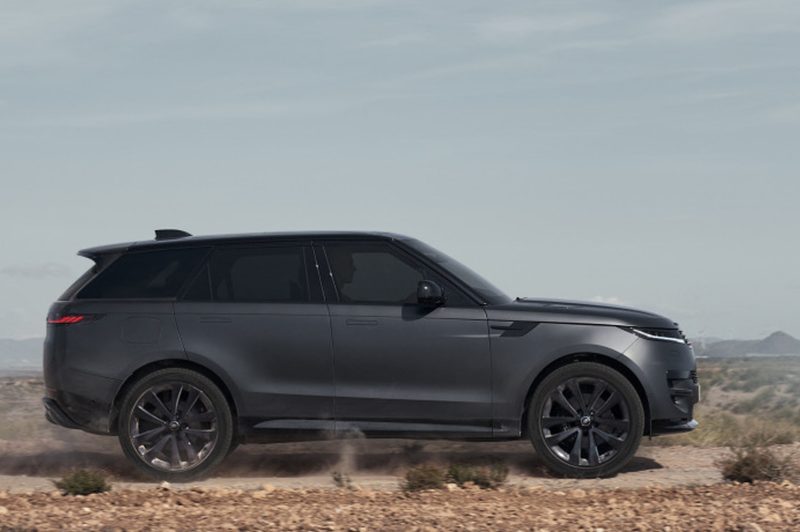 Right side profile shot of a 2025 Range Rover Sport Dynamic SE with Stealth Pack driving on a desert road with mountains in the background.