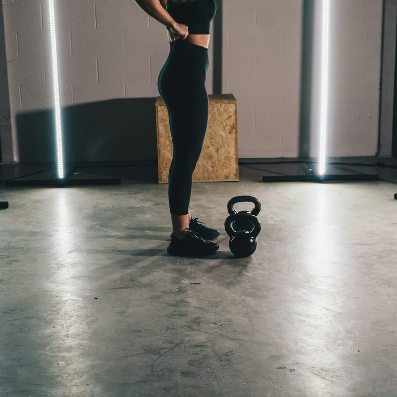 Woman wearing leggings standing in gym next to kettlebell
