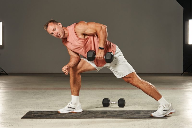 Oone-arm dumbbell row in a bent-over position with emphasis on the leg by an athlete in shorts and a T-shirt