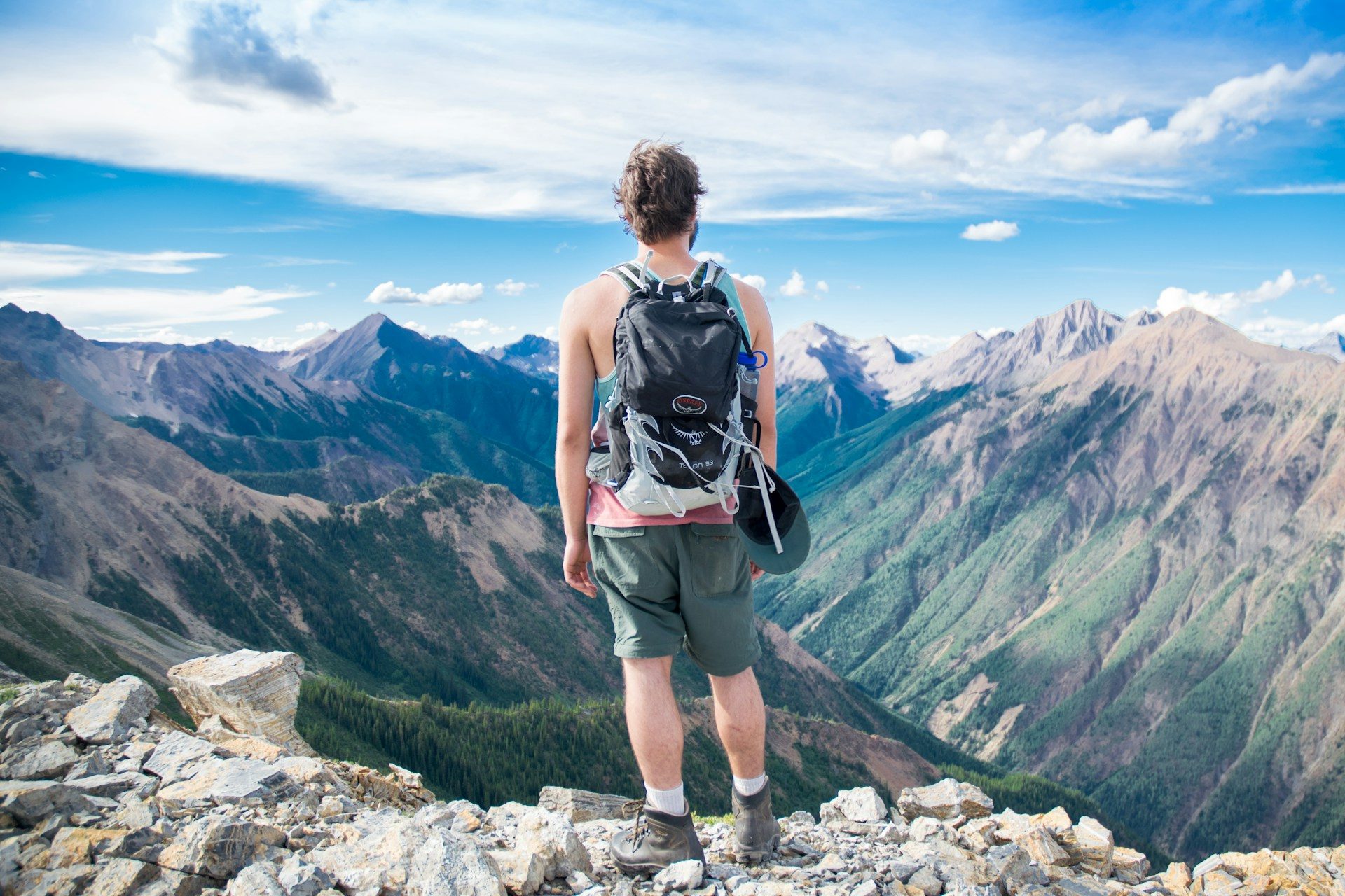 A man looking down into a valley, enjoying the fresh air and taking a pause from a hike.