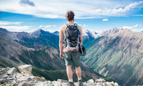 A man looking down into a valley, enjoying the fresh air and taking a pause from a hike