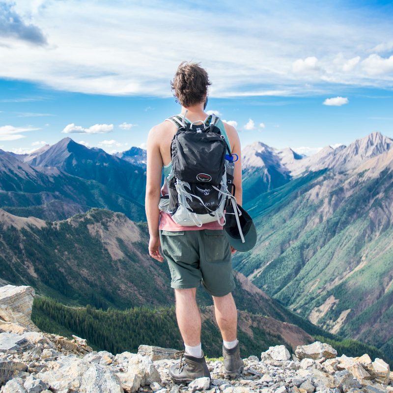 A man looking down into a valley, enjoying the fresh air and taking a pause from a hike