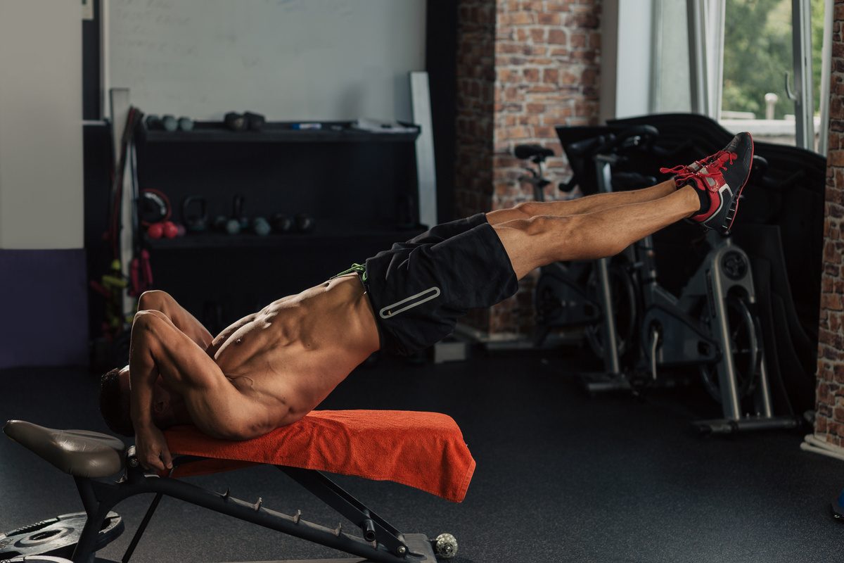 Young muscular fit man in the gym doing dragon flag abs exercise on a bench