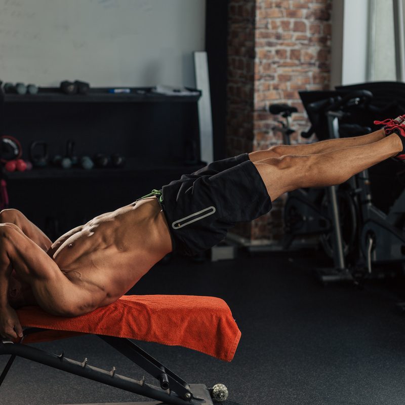 Young muscular fit man in the gym doing dragon flag abs exercise on a bench