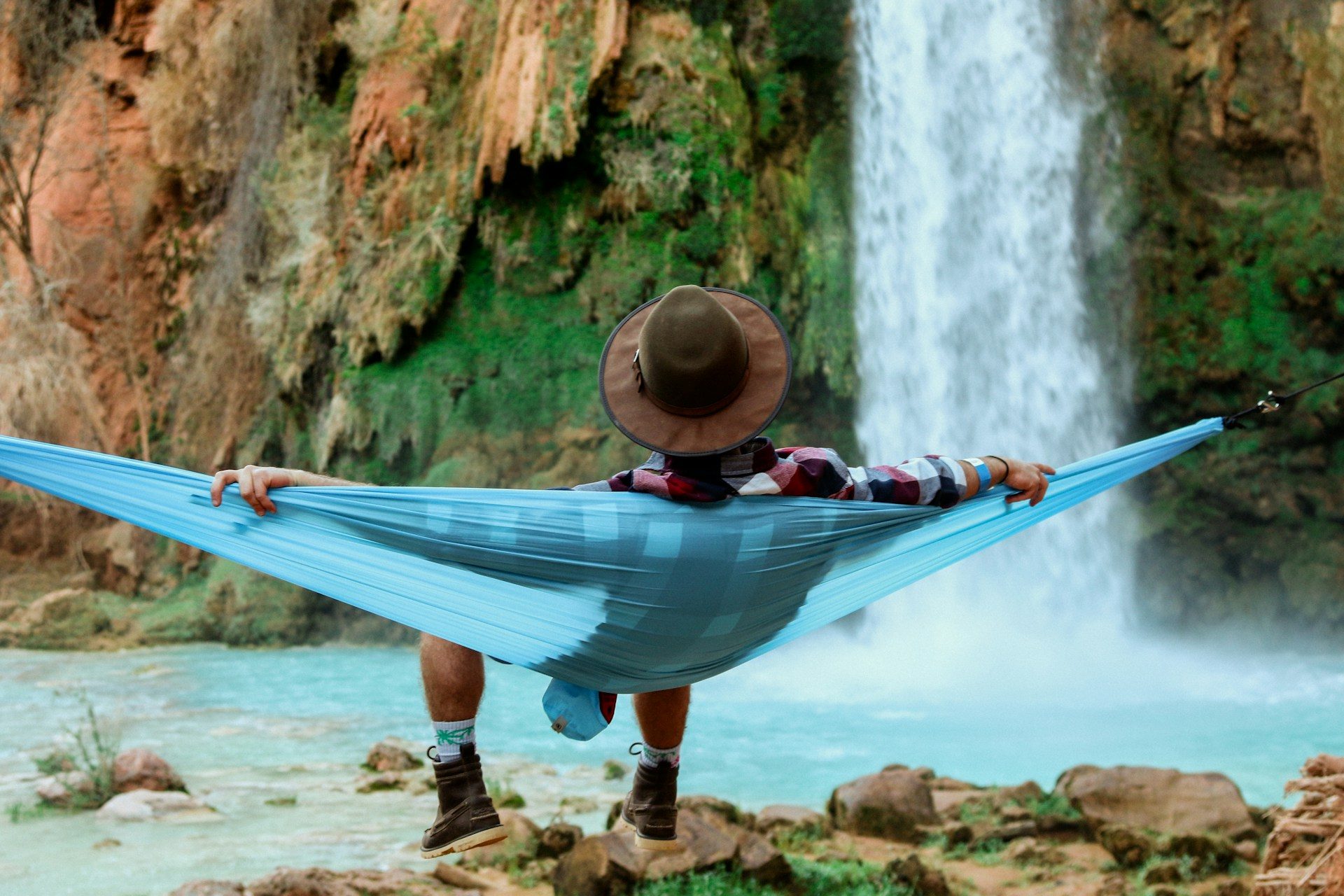 A man laying in a hammock enjoying a waterfall and pool of water