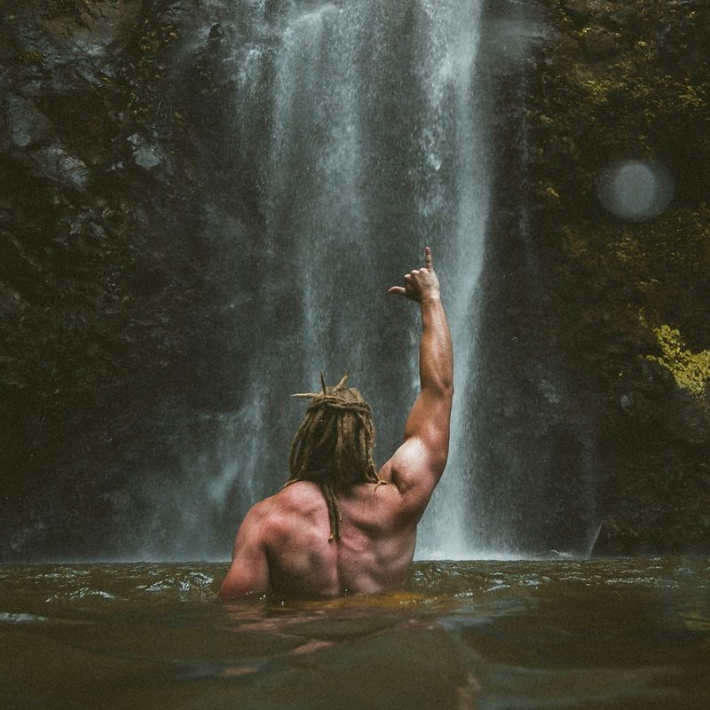 Shirtless man fist in the air punching air by a waterfall outside in nature back muscles