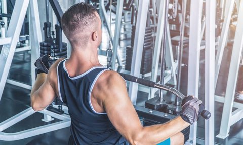 Muscular man using pull-down machine in the gym