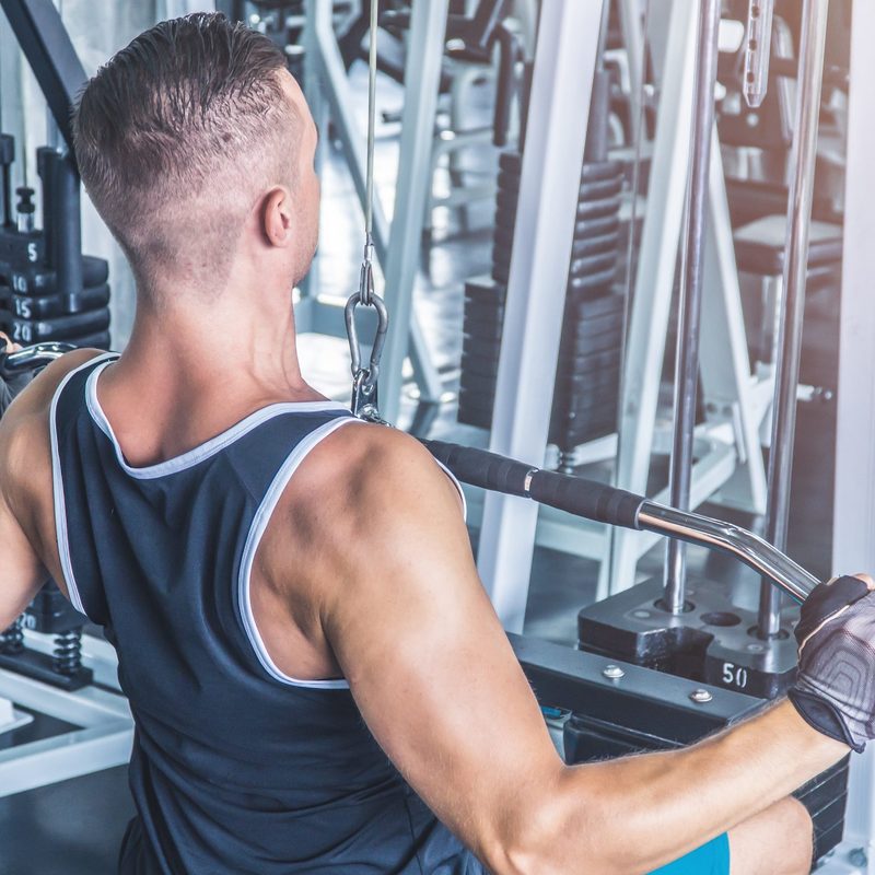 Muscular man using pull-down machine in the gym