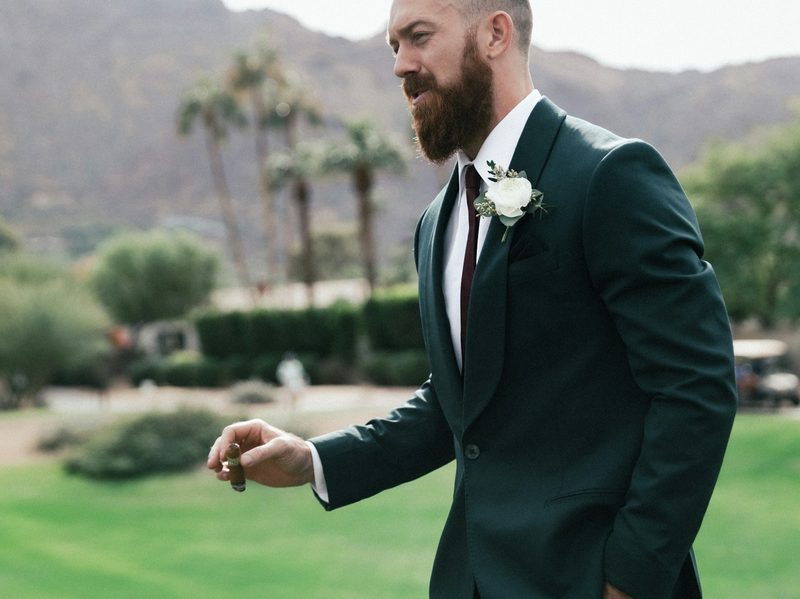 Man in a tux at a wedding holding a lit cigar.