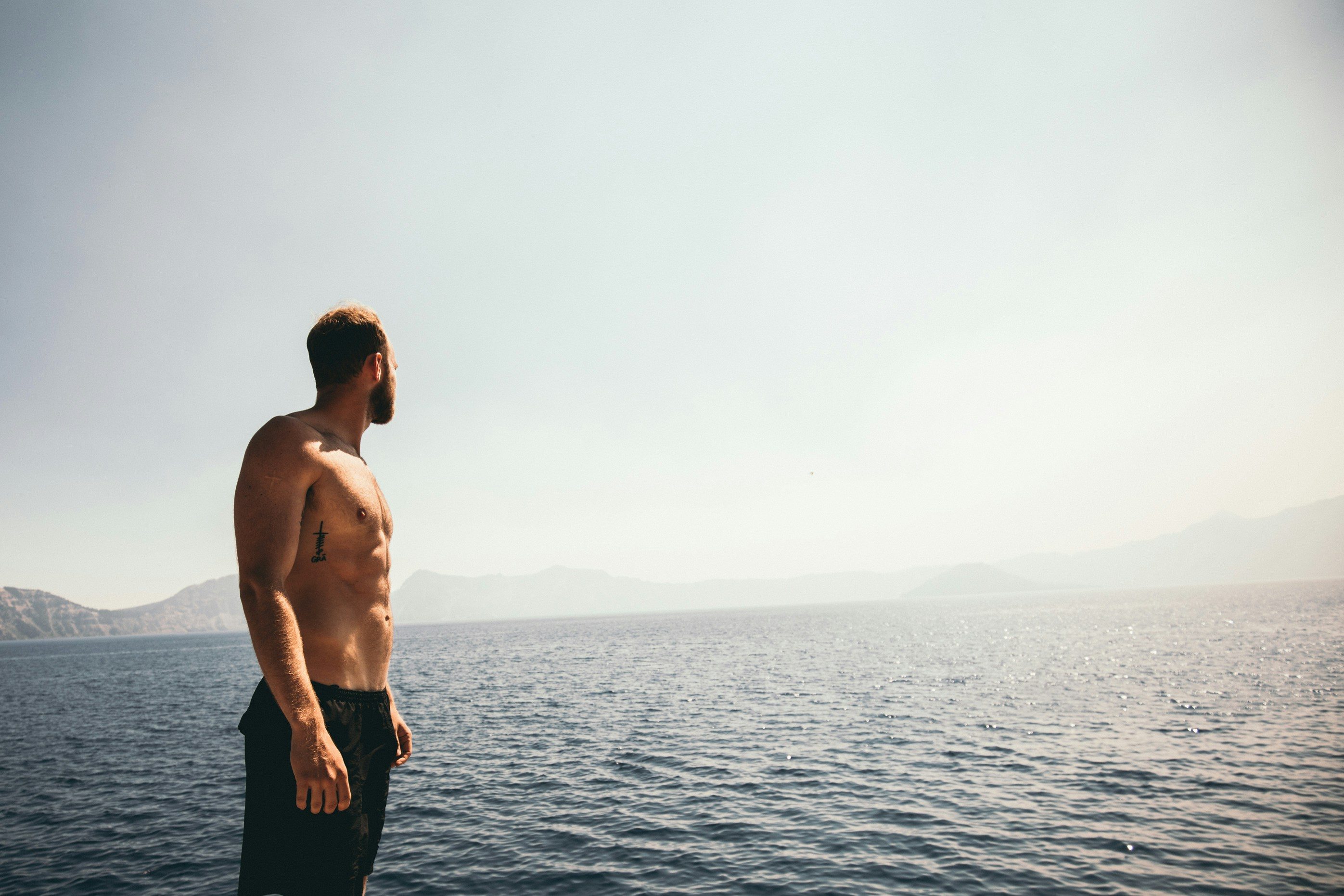 a topless man standing by the water