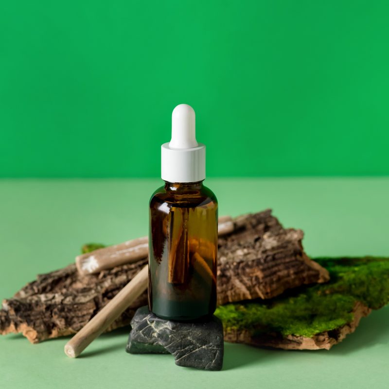 Serum Glass Bottle Green Background Composition with Natural Materials: Tree Bark, Stones Wooden Sticks Health and Natural Care Cosmetics Concept