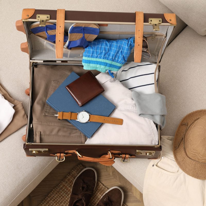Open suitcase with different men clothes and accessories on sofa, top view