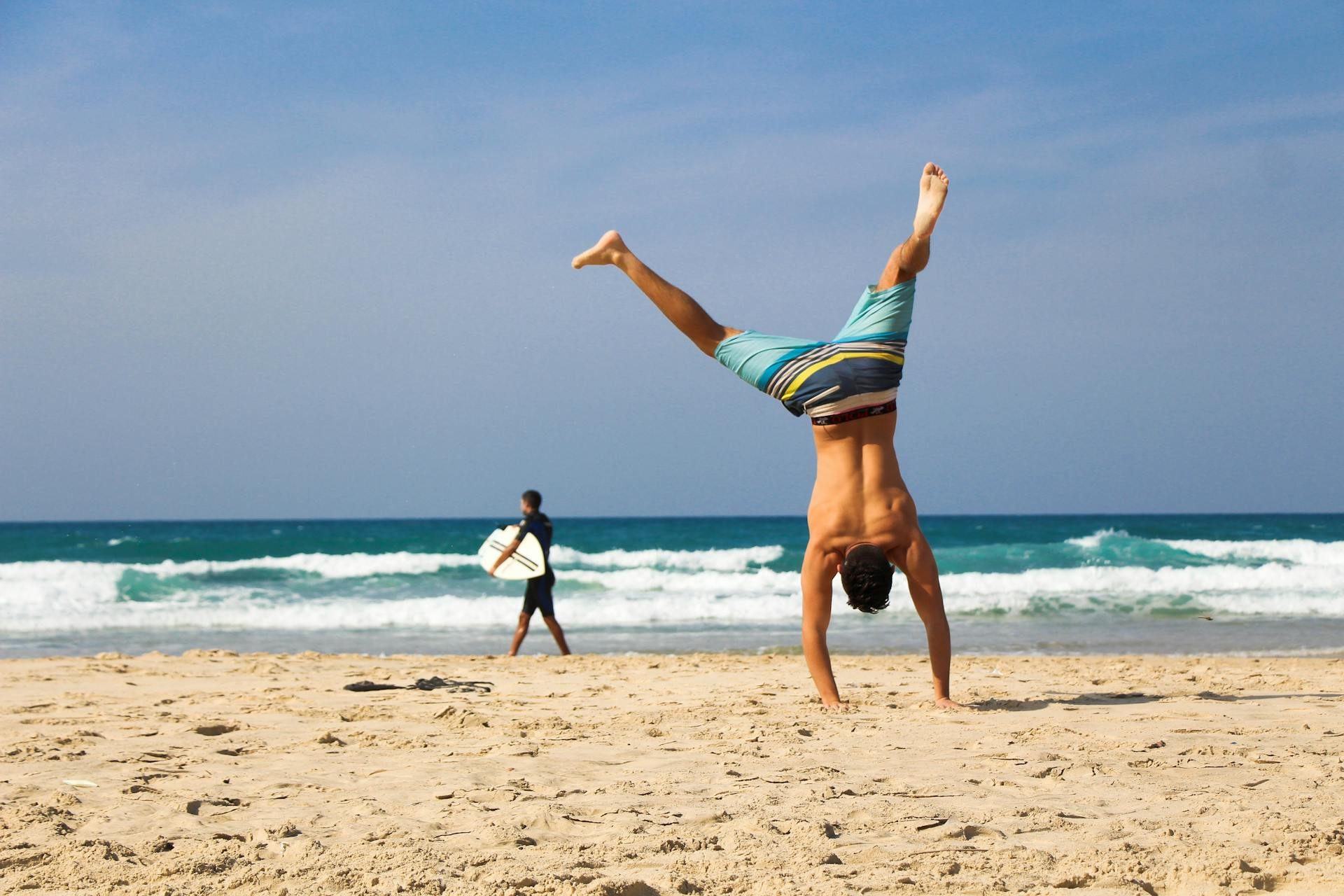 man at beach handstand surfer in background near ocean