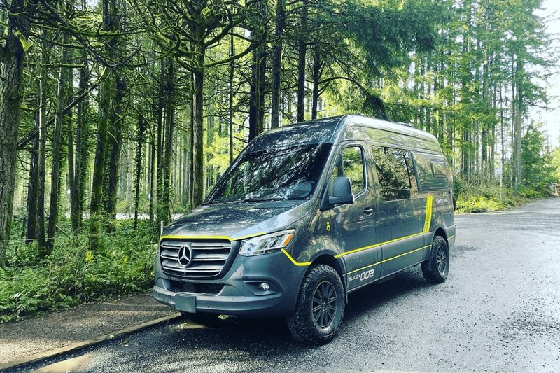A Remote Vans camper van parked on a street in a wooded area.