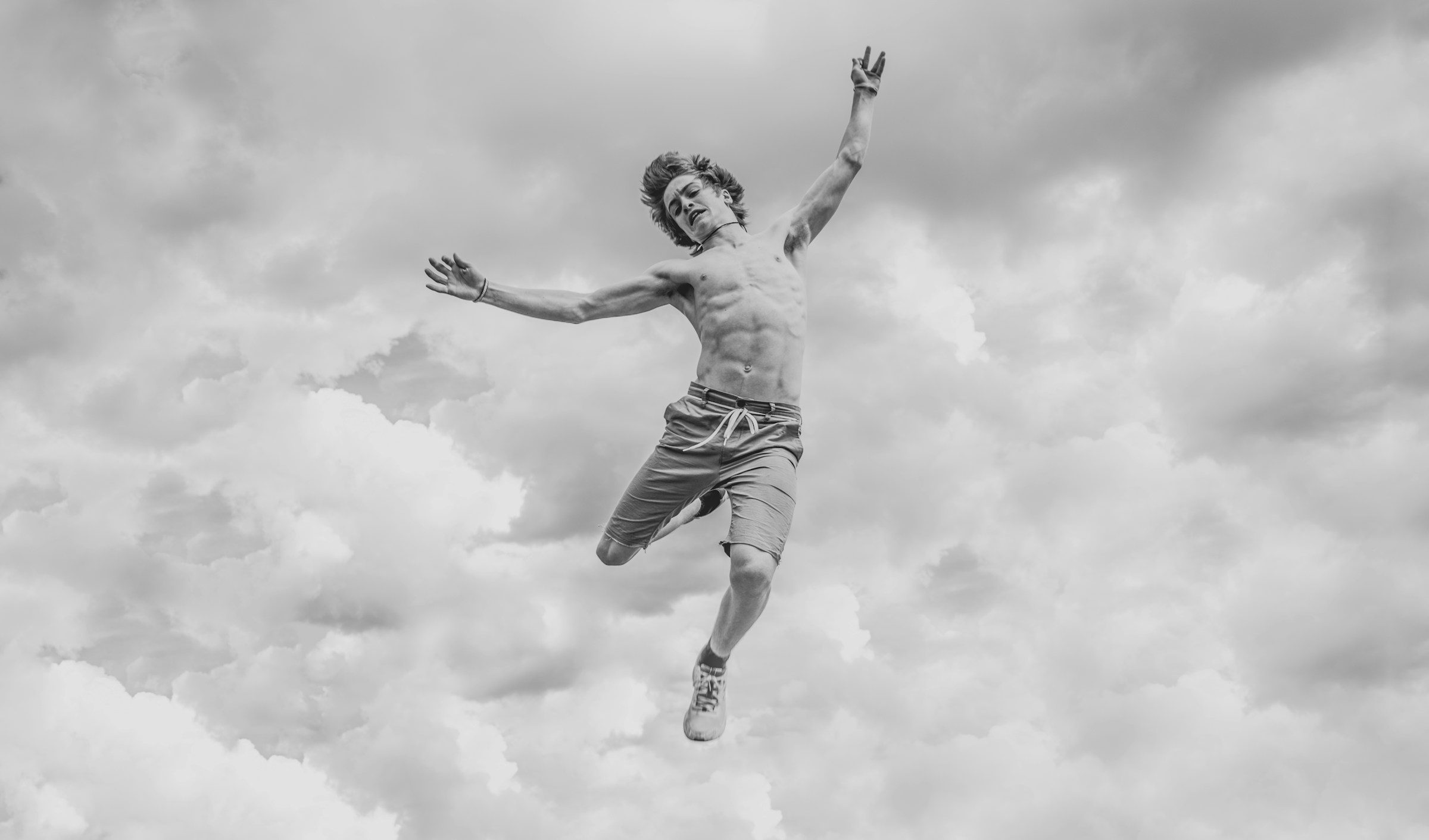 man jumping high in the air black and white shirtless cloud