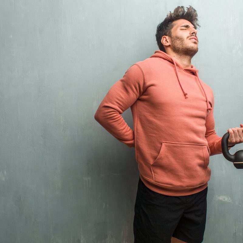 Man holding a weight while showing some pain the back area