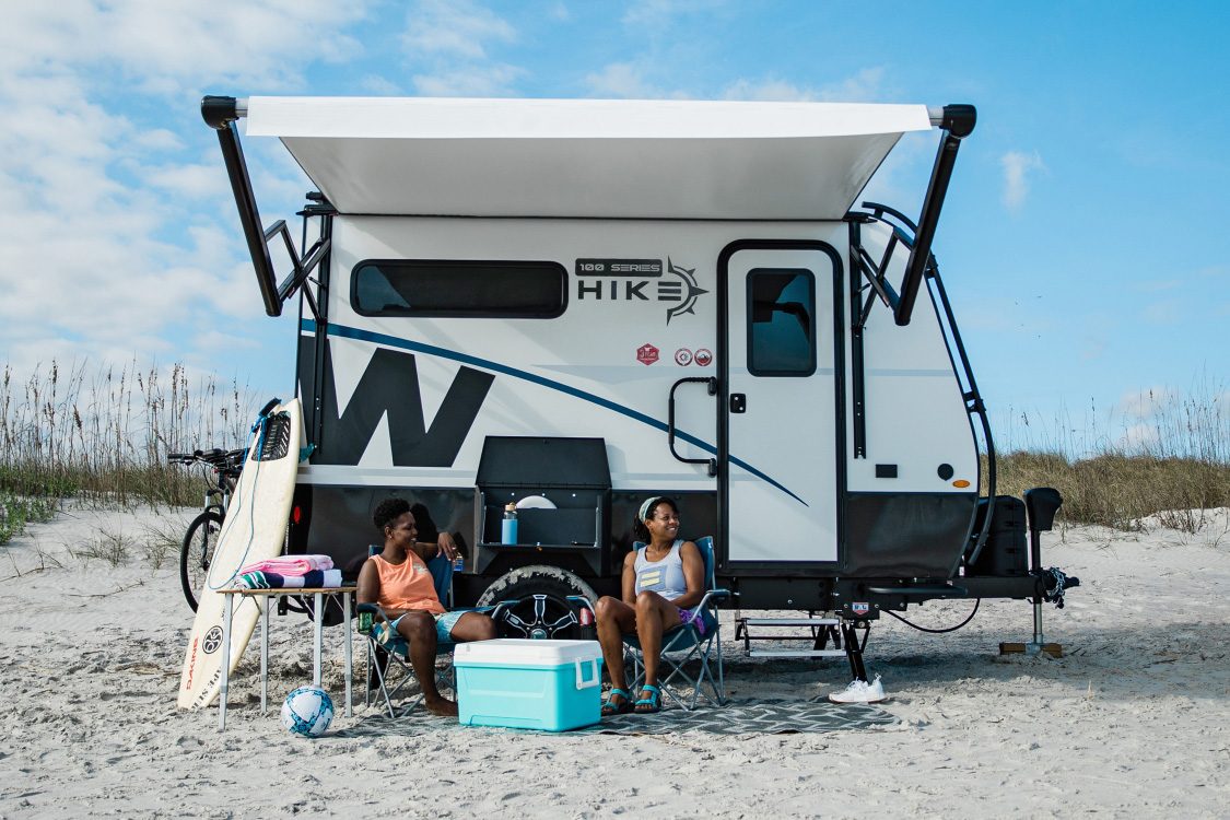 Couple sitting outside a Winnebago Hike 100 off-road trailer parked on the beach.