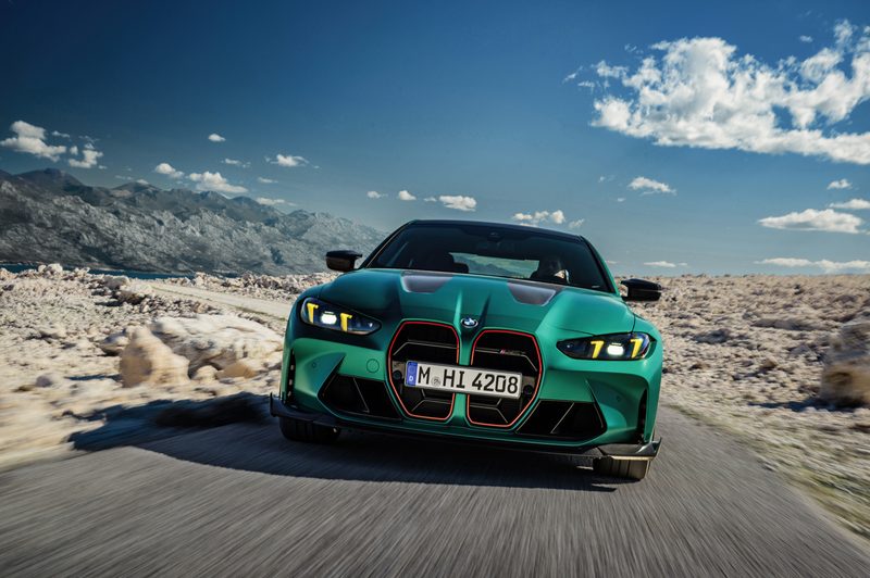 2025 BMW M4 CS driver direct frontal shot driving on single-lane blacktop in a rocky desert setting with mountains in the background.